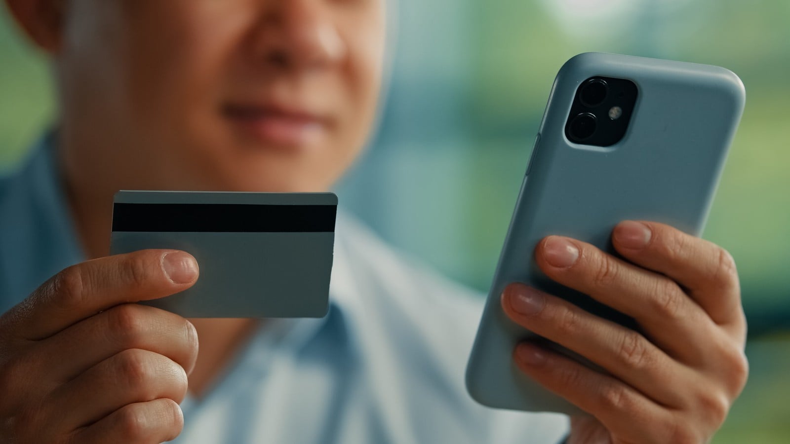 A man holding a payment card in one hand and a phone in the other